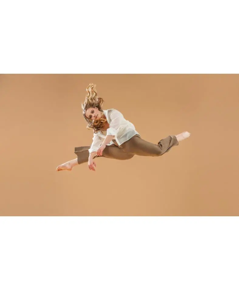 Woman dancer leaping mid-air against beige background
